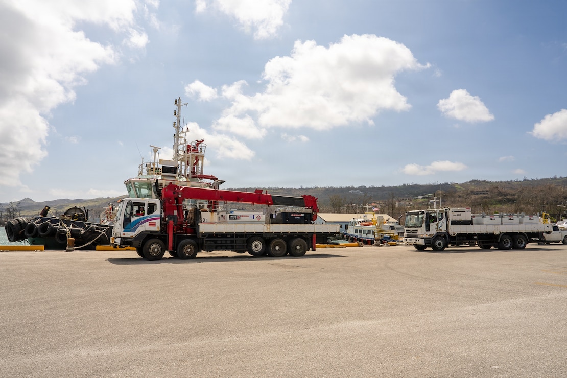 Two flatbed trucks are loaded with generators at a port in Saipan