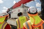 Three individuals look at a generator which is sitting on a flatbed truck.