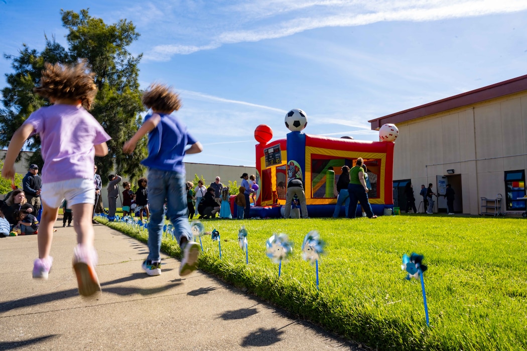 Children run near a bouncy castle, the grass is green and there are pinwheels blowing in the wind.