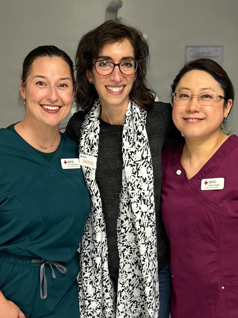 Mrs. Regina Kosiba (center), lead volunteer for the American Red Cross Dental Program, stands with dental assistant students Mrs. Anna Mendeola (left) and Mrs. Chloe Osada (right) during the Red Cross Dental Assistant Training Program at Tignor Dental Clinic on Joint Base Langley-Eustis, Virginia.