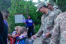 Airman hands a button pin to a child for Purple Up Day.