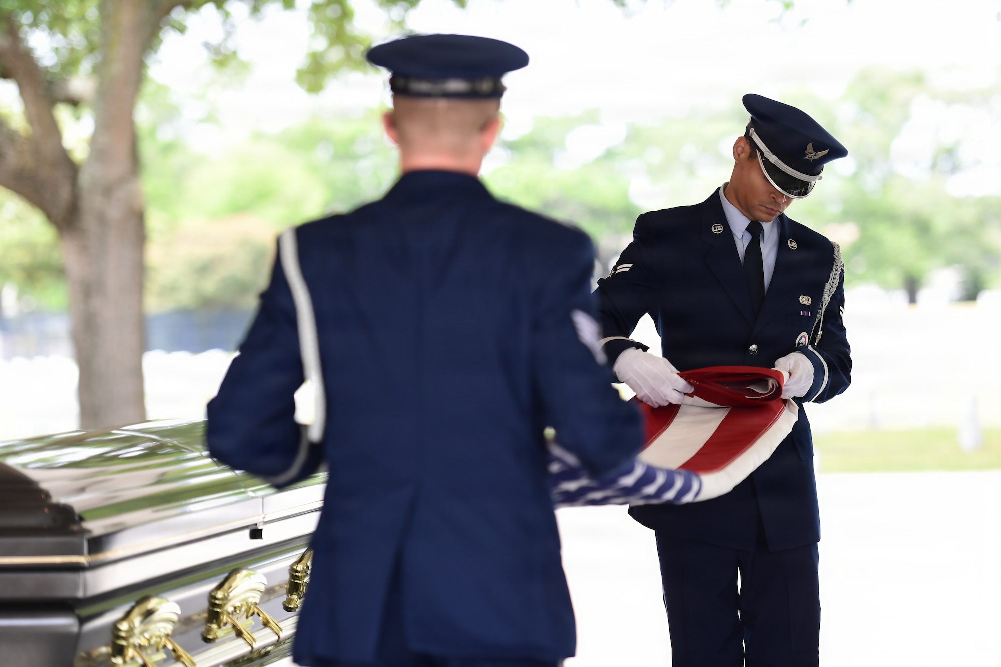 Two military members fold a U.S. flag during a funeral.