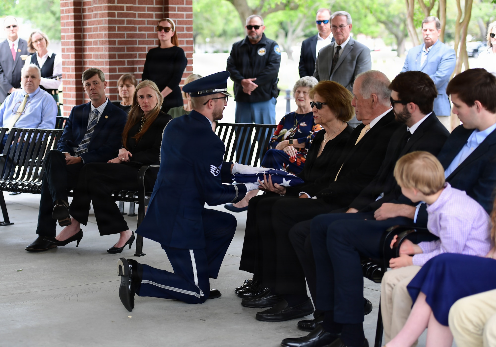 A man in military uniform presents a folded U.S. Flag to a family member of the deceased.
