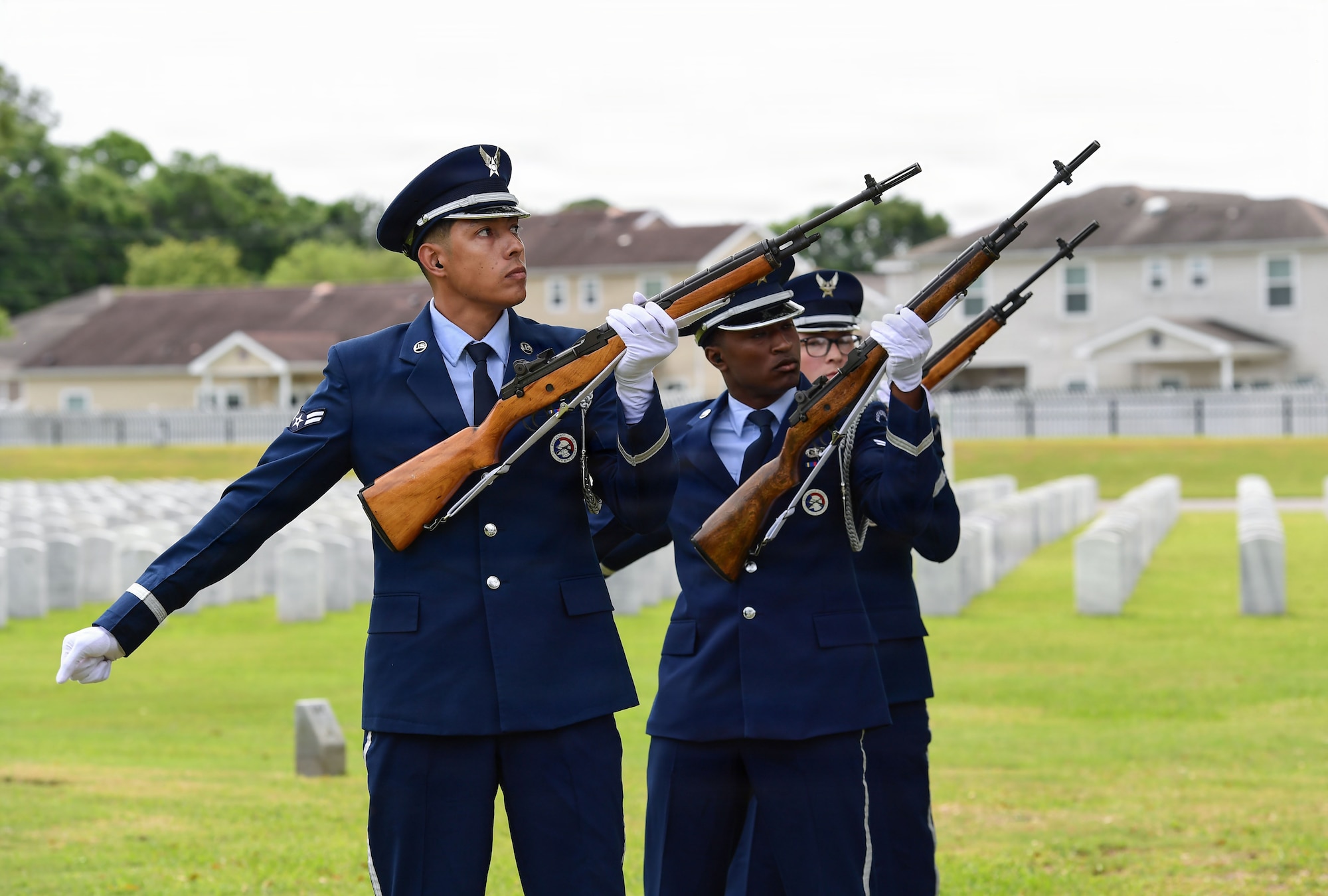 Three military members fire rifles during a funeral.