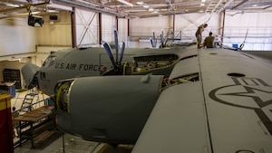 Airmen sit on top of a C-130H Hercules aircraft in safety harnesses performing an inspection.