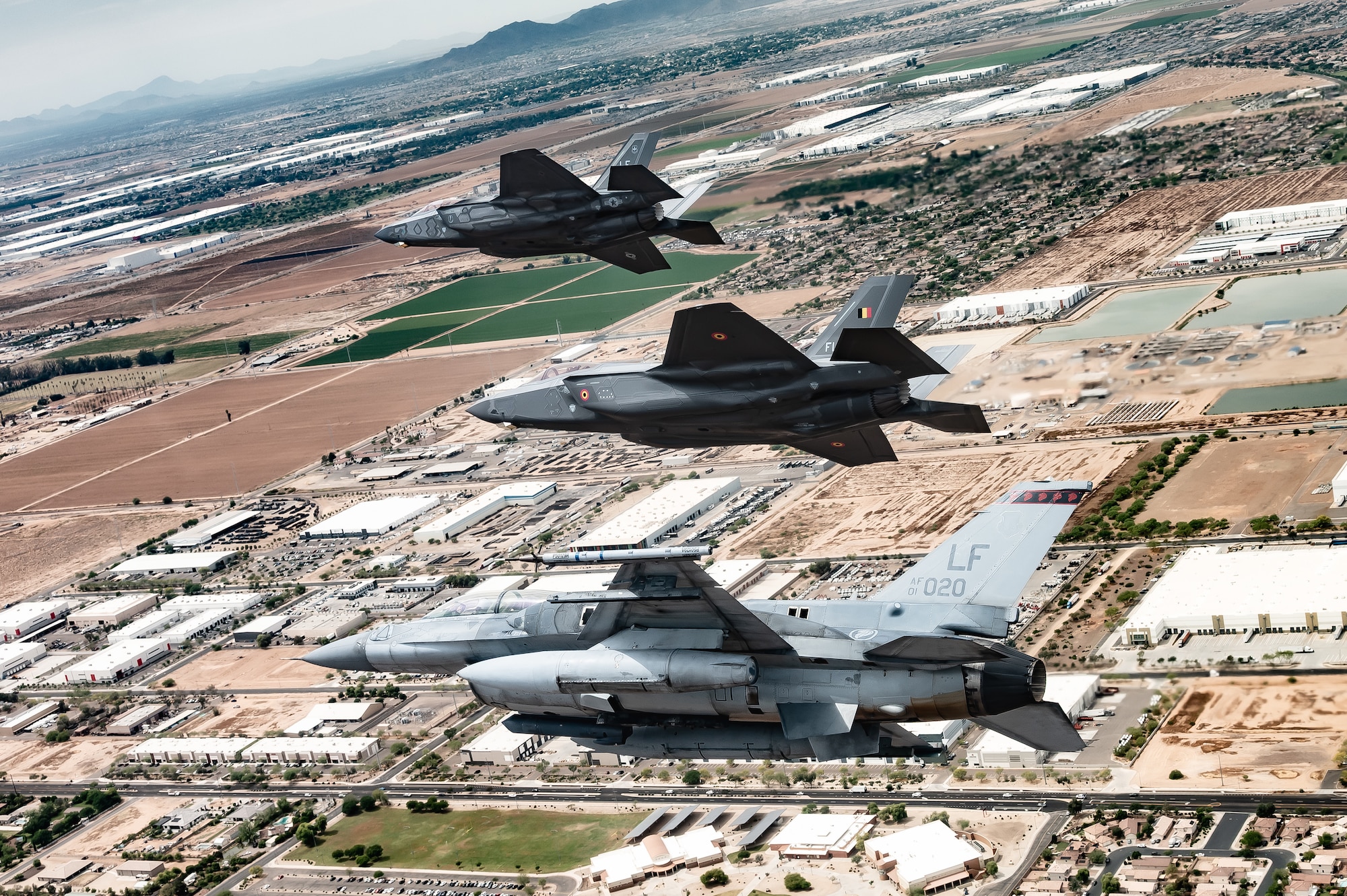 A Republic of Singapore Air Force F-16D Fighting Falcon, bottom, a Belgian Air Component F-35A Lightning II, middle, and U.S. Air Force F-35A Lightning II, top, bank over the Arizona landscape