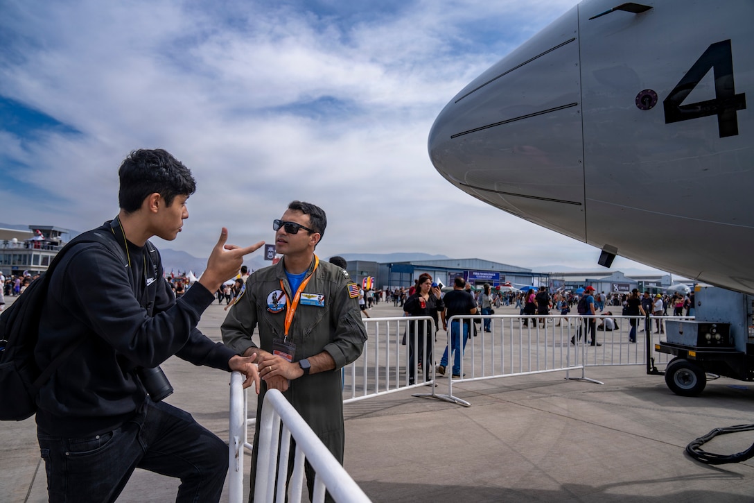 U.S. Navy Lt. Marshad Huq, Patrol Squadron Thirty P-8A Poseidon aircraft commander, right, talks to an event attendee about military patches during Feria Internacional del Aire y del Espacio (FIDAE) 2026 in Santiago, Chile, April, 2026. The P-8 static display provided an opportunity for the U.S. military to engage with the public and share information about U.S. aviation and defense technology. (U.S. Air Force photo by Andrea Jenkins)
