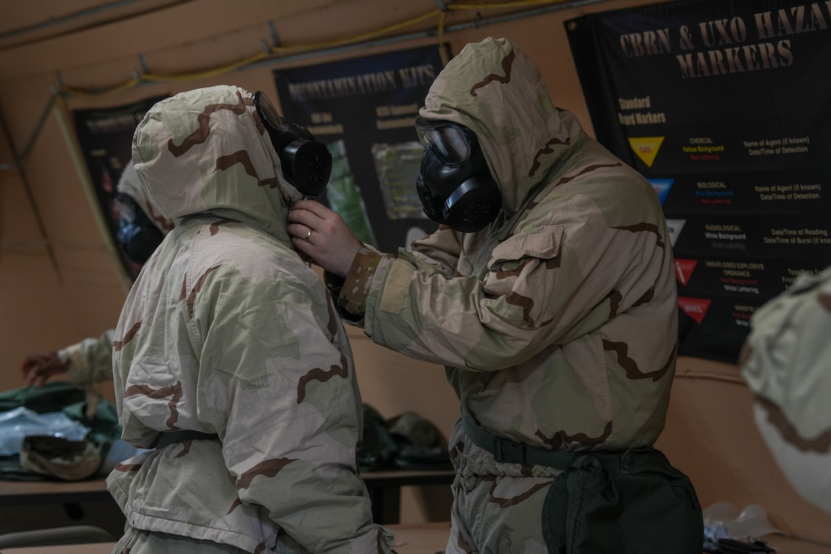 An Airman helps another Airman tighten his gas mask