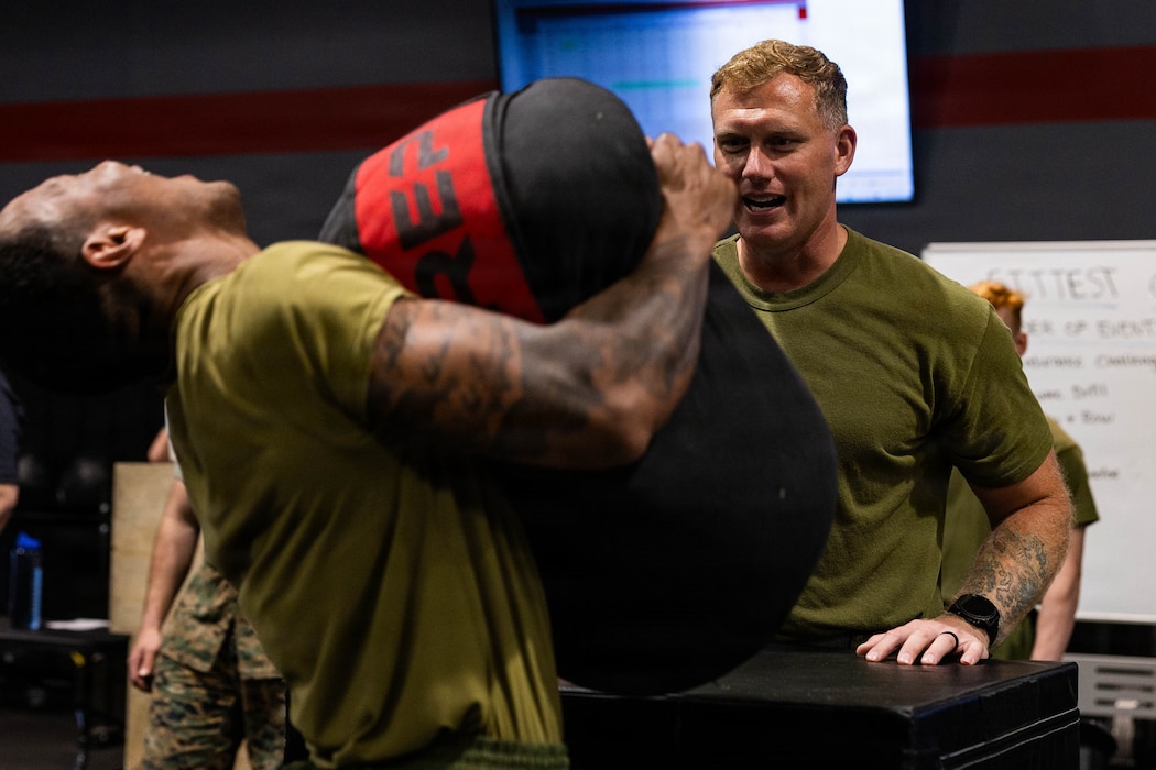 U.S. Navy Hospital Corpsman 1st Stephen Bubenko, right, staff noncommissioned officer in charge of the 2nd Marine Logistics Group Human Performance Center, cheers on a U.S. Marine during a sandbag shuttle run as part of a Fittest of the MLG competition hosted by the 2nd MLG HPC at Marine Corps Base Camp Lejeune, North Carolina, April 17, 2026. Twice a year, teams from across 2nd MLG's battalions compete for the title of “Fittest of the MLG” to promote physical fitness, camaraderie, and friendly competition. (U.S. Marine Corps photo by Lance Cpl. Isabella Ramos)