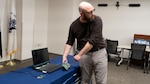 This photo shows Dr. Husted demonstrating key tools for Electromagnetic Spectrum Operations Research. The laptop is a Navy Research Enterprise Network (NREN) laptop running Visual Studio Code and Windows Subsystem for Linux with capability to remotely connect to his NREN Linux desktop. This platform allows him to develop capabilities using the Ettus Software Defined Radio (in his hands) and the Open Source Radiona Field Programmable Gate Array (FPGA) board on the table. These capabilities combined provide the fundamental enabler of enhancing the non-kinetic lethality of our men and women in uniform.