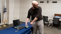 This photo shows Dr. Husted demonstrating key tools for Electromagnetic Spectrum Operations Research. The laptop is a Navy Research Enterprise Network (NREN) laptop running Visual Studio Code and Windows Subsystem for Linux with capability to remotely connect to his NREN Linux desktop. This platform allows him to develop capabilities using the Ettus Software Defined Radio (in his hands) and the Open Source Radiona Field Programmable Gate Array (FPGA) board on the table. These capabilities combined provide the fundamental enabler of enhancing the non-kinetic lethality of our men and women in uniform.