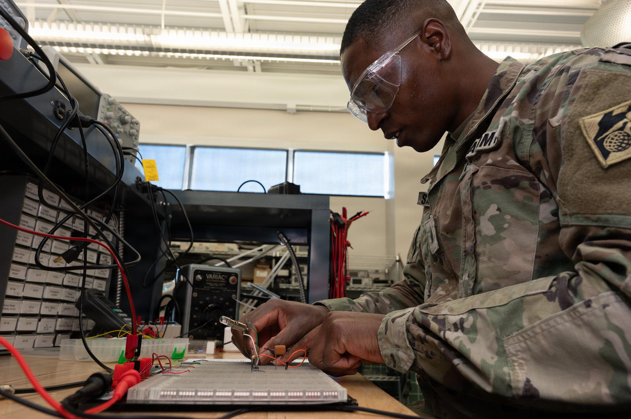 A soldier works on a piece of electrical gear at a workbench.