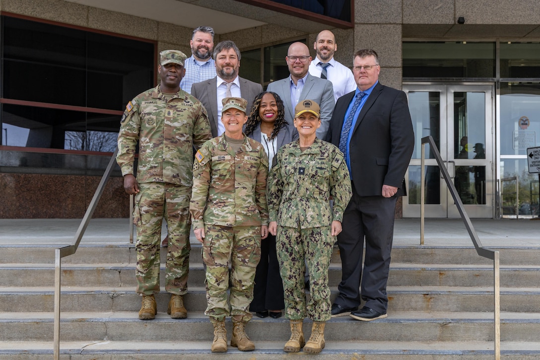 A group of smiling people stand on the front steps of a building.