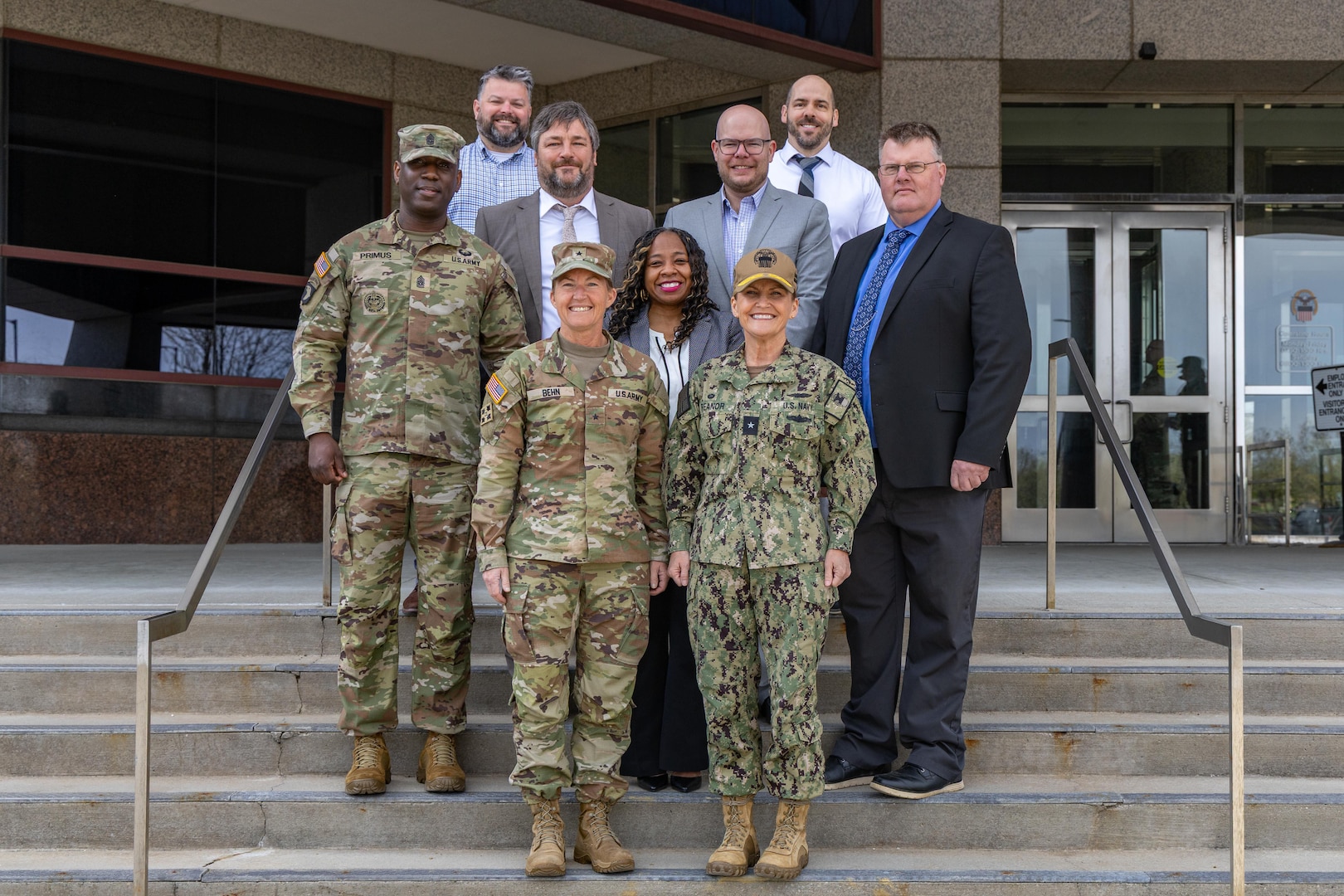 A group of smiling people stand on the front steps of a building.
