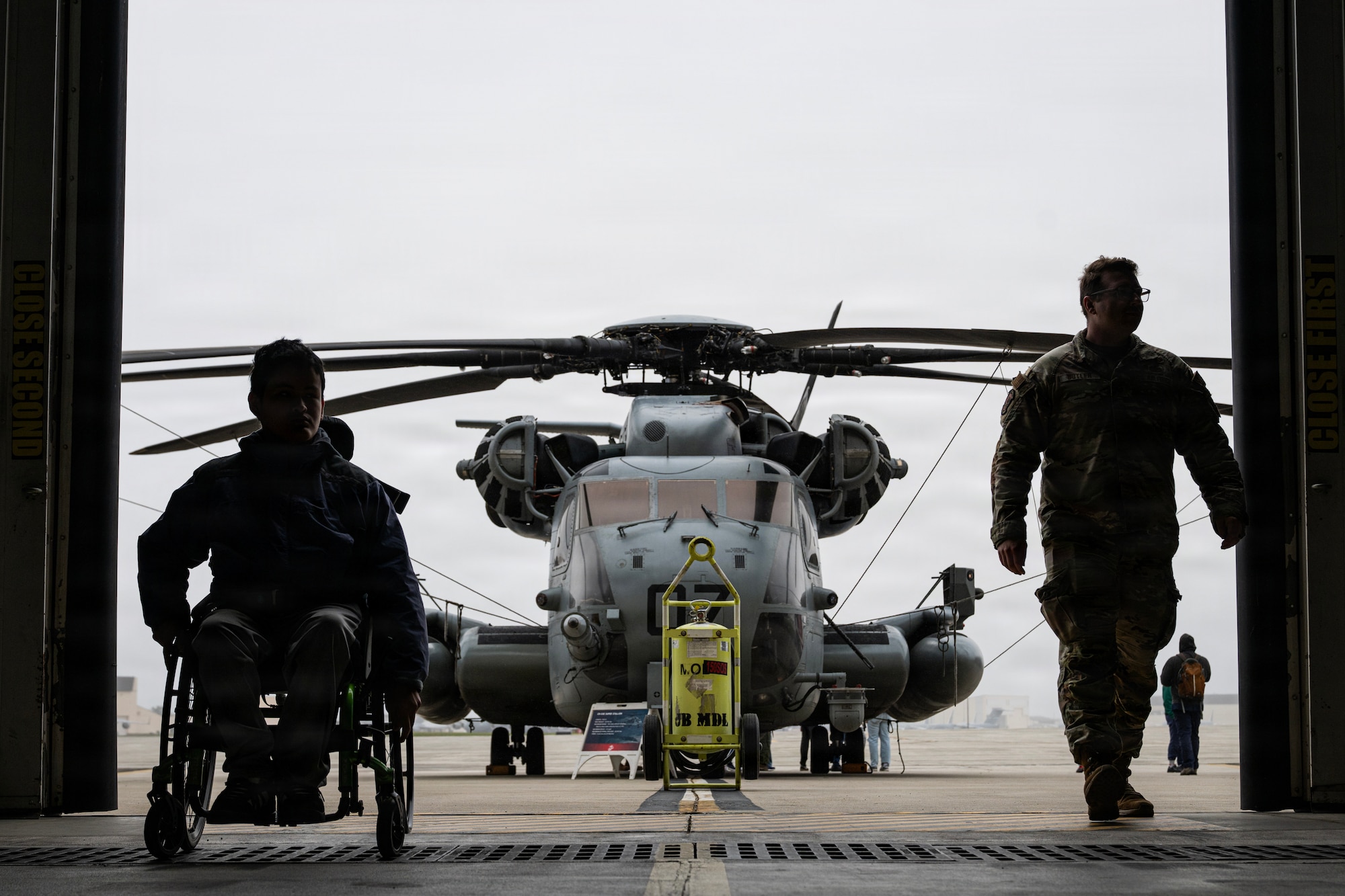 A student attending Mercer County Special Services School District, and U.S. Air Force Tech. Sgt. Joshua Butler, 321st Contingency Response Squadron contracting officer, enter a hangar in front of a U.S. Marine Corps CH-53E Super Stallion at the Special Needs Airshow, April 2, 2026 at Joint Base McGuire-Dix-Lakehurst, New Jersey.