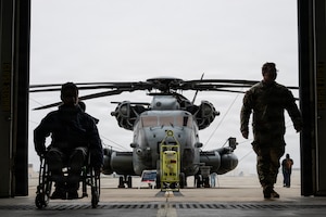 A student attending Mercer County Special Services School District, and U.S. Air Force Tech. Sgt. Joshua Butler, 321st Contingency Response Squadron contracting officer, enter a hangar in front of a U.S. Marine Corps CH-53E Super Stallion at the Special Needs Airshow, April 2, 2026 at Joint Base McGuire-Dix-Lakehurst, New Jersey.