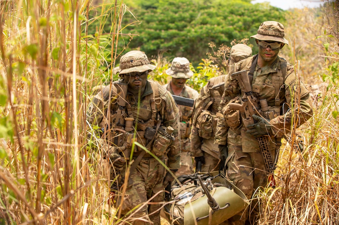 Soldiers carrying a mannequin walk through tall grass.