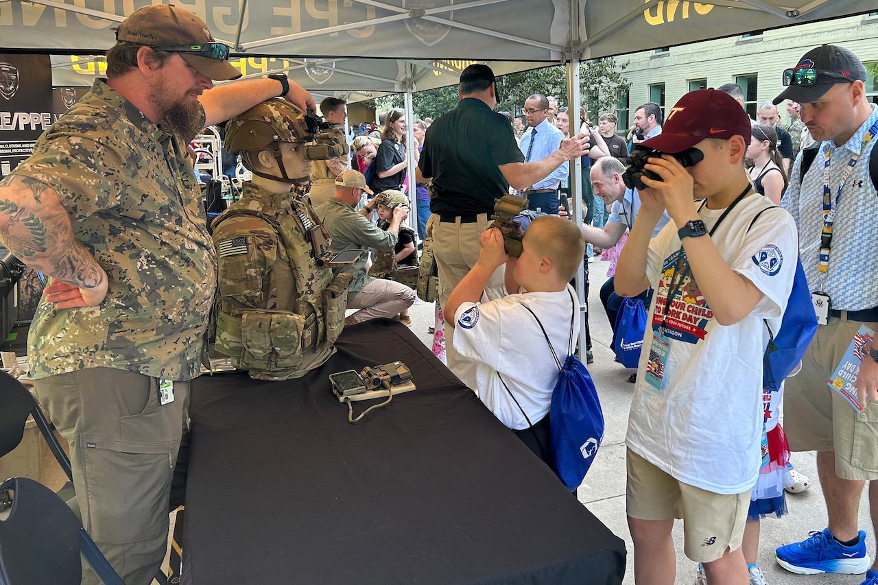 Two boys look though goggles. An older man watches them.