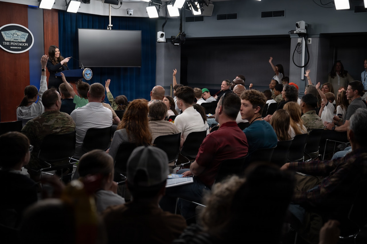 A person stands at a lectern as people in an audience sit in the foreground.