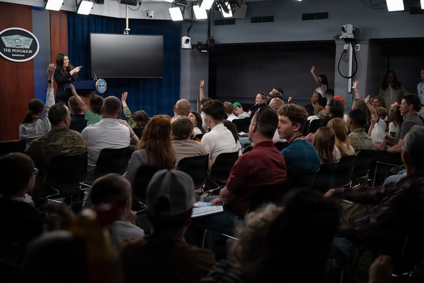 A person stands at a lectern as people in an audience sit in the foreground.