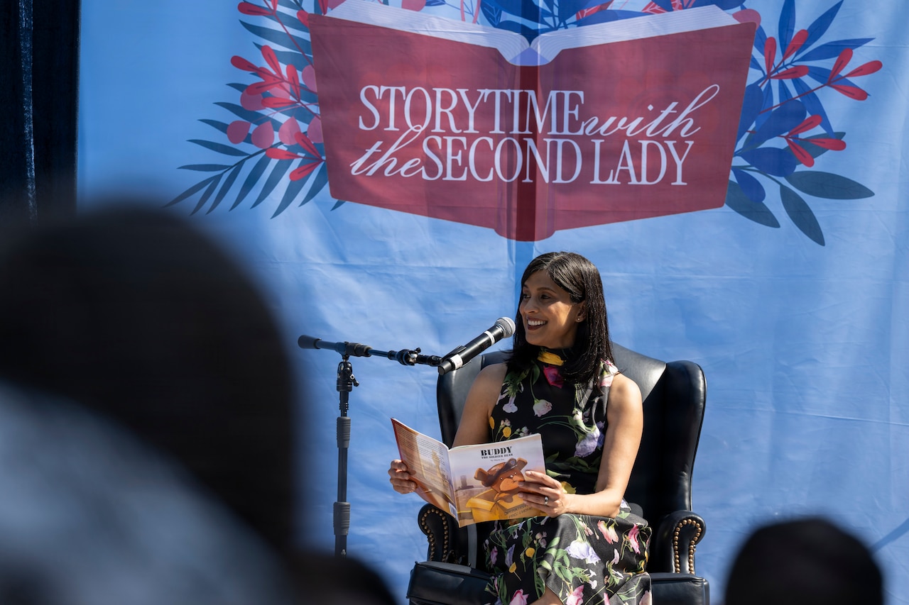 A person in civilian attire holds and reads a book in front of a banner that reads "Storytime with the Second Lady."