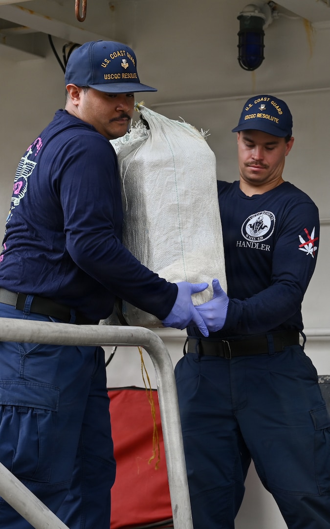 Two Coast Guard Cutter Resolute (WMEC 620) crew members pass a bale of cocaine during a drug offload at Base Miami Beach, Florida, April 23, 2026. The offload is a result of three suspected drug smuggling interdictions in the Caribbean Sea, weighing approximately 2,570 pounds, and worth an estimated $19.3 million (U.S. Coast Guard photo by Petty Officer 3rd Class Reese Hindmarsh)