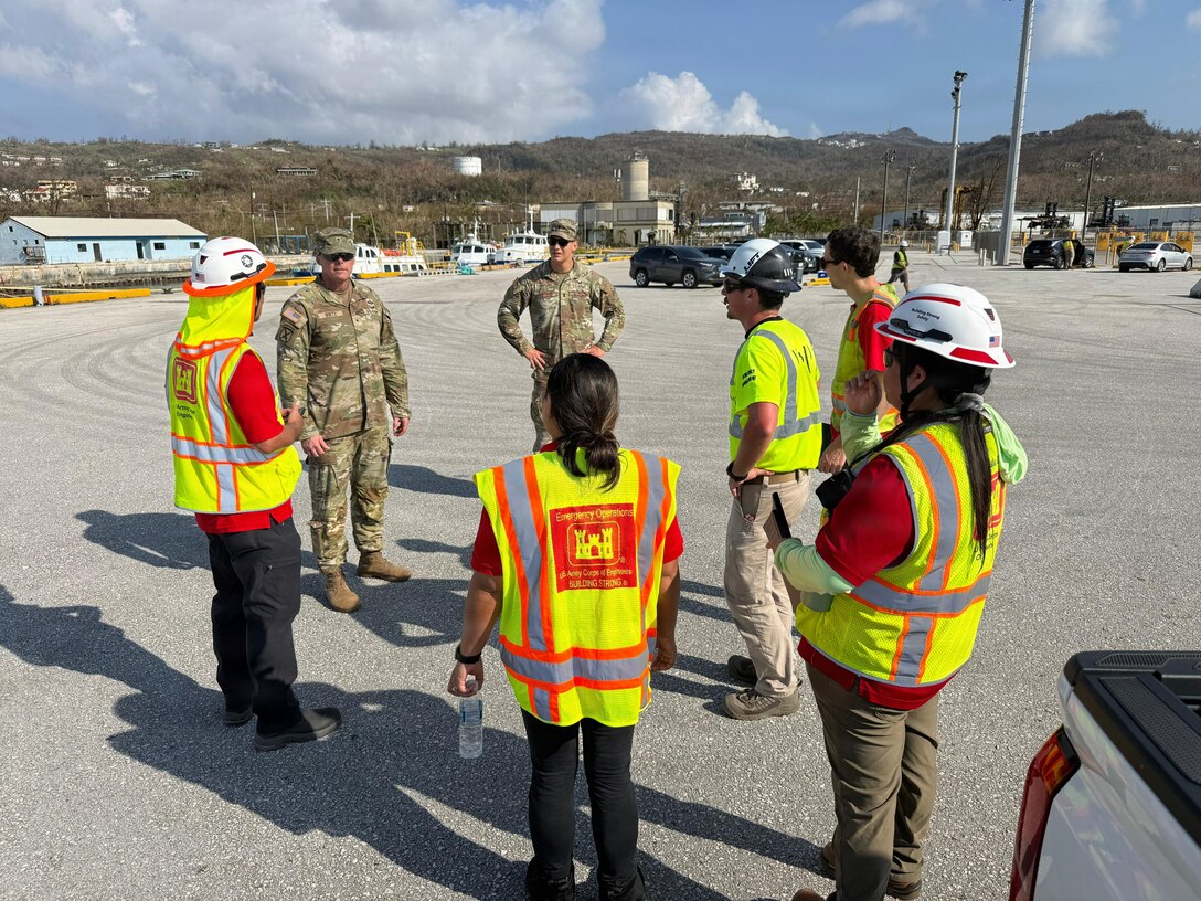 Two Soldiers are seen talking to a group of people in hard hats and safety vests.