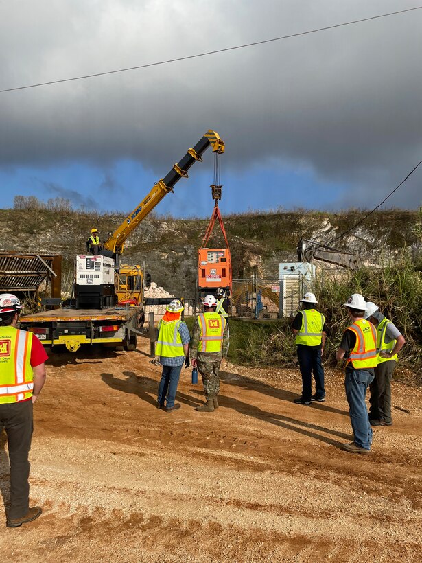 a group of people watch a crane hoist a generator.
