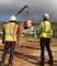 two men watch as a crane lifts a generator off the ground.