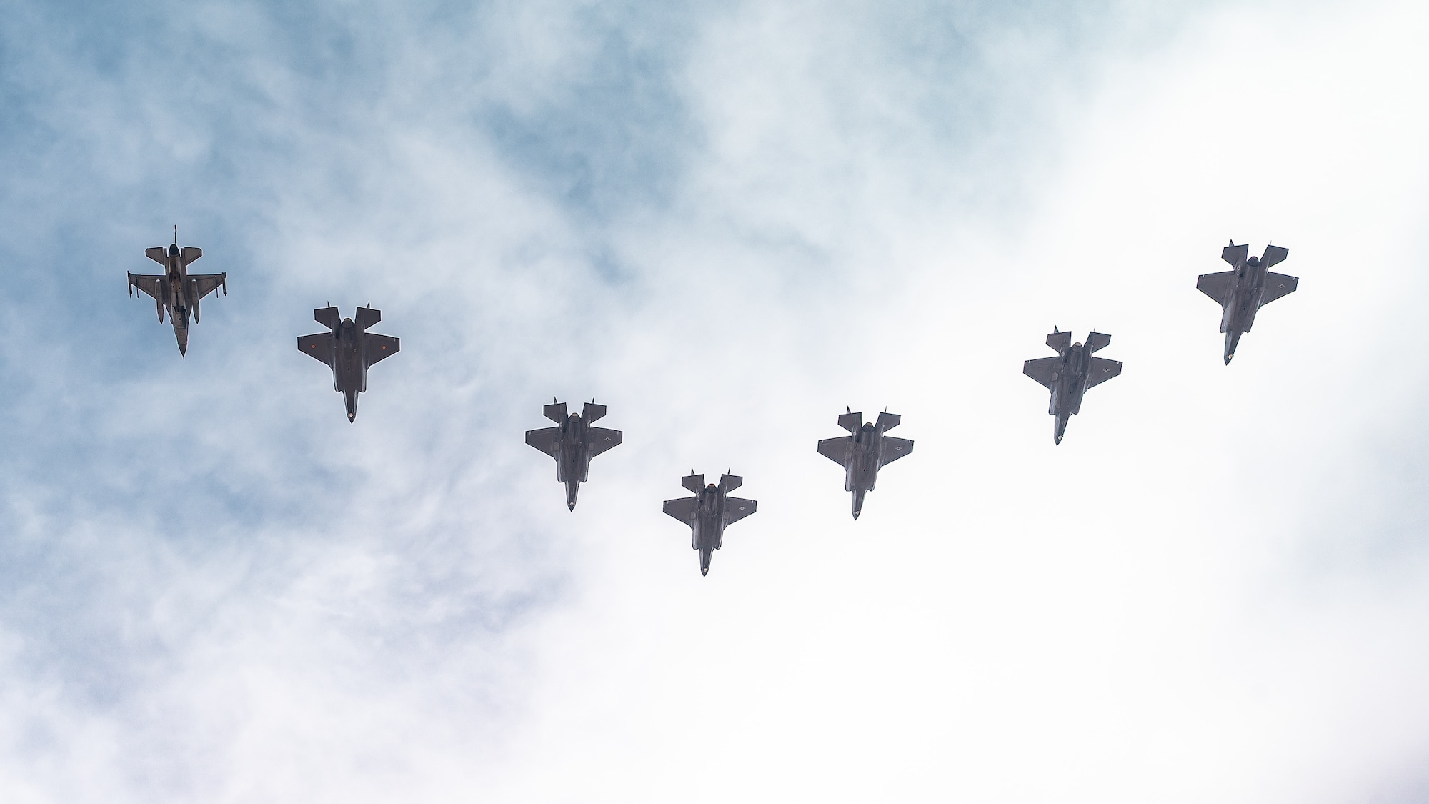 A Republic of Singapore Air Force F-16D Fighting Falcon, a Belgian Air Component F-35A Lightning II, and U.S. Air Force F-35A Lightning II aircraft assigned to the 56th Fighter Wing soar overhead in a seven-ship formation