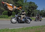 Motorcyclists ride by the P-40 static display during a 2024 Motorcycle Mentorship Ride at Hanscom Air Force Base, Mass. The theme for this year’s preseason is “Year of the Mentor,” established by the Air Force Safety Center. (U.S. Air Force photo by Todd Maki)