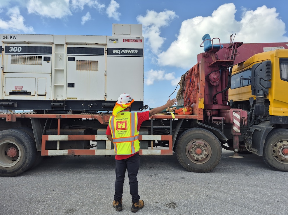 a man directs a truck with large generators loaded on the back.