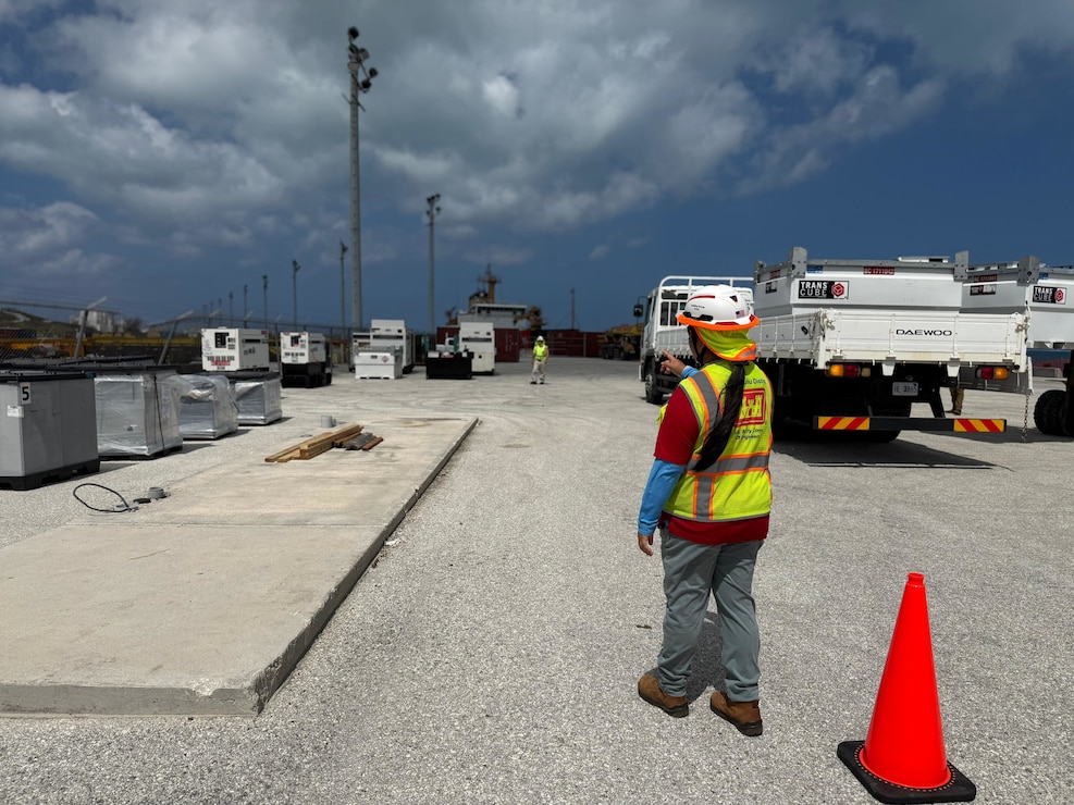 An individual is next to a traffic cone pointing at generators in the distance.