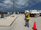 An individual is next to a traffic cone pointing at generators in the distance.