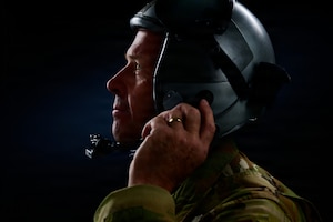 A close-up image of a pilot standing in silhouette as he adjusts his helmet.