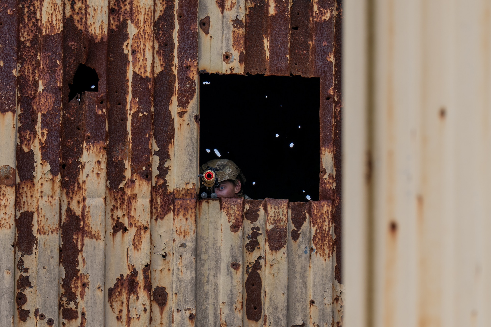 Man sits in the window, looking through a scope.