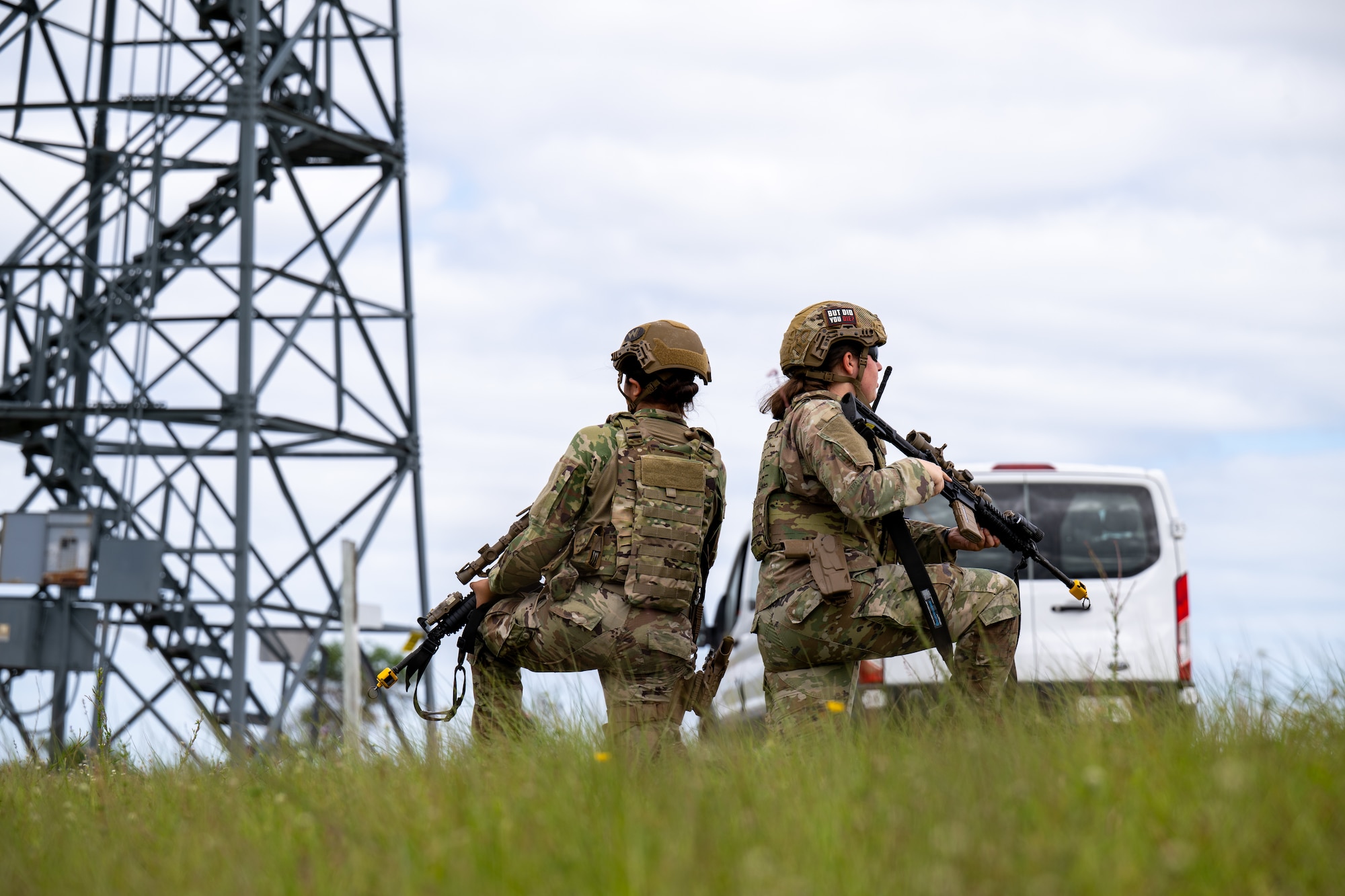 Two women take a knee back to back and survey the area.