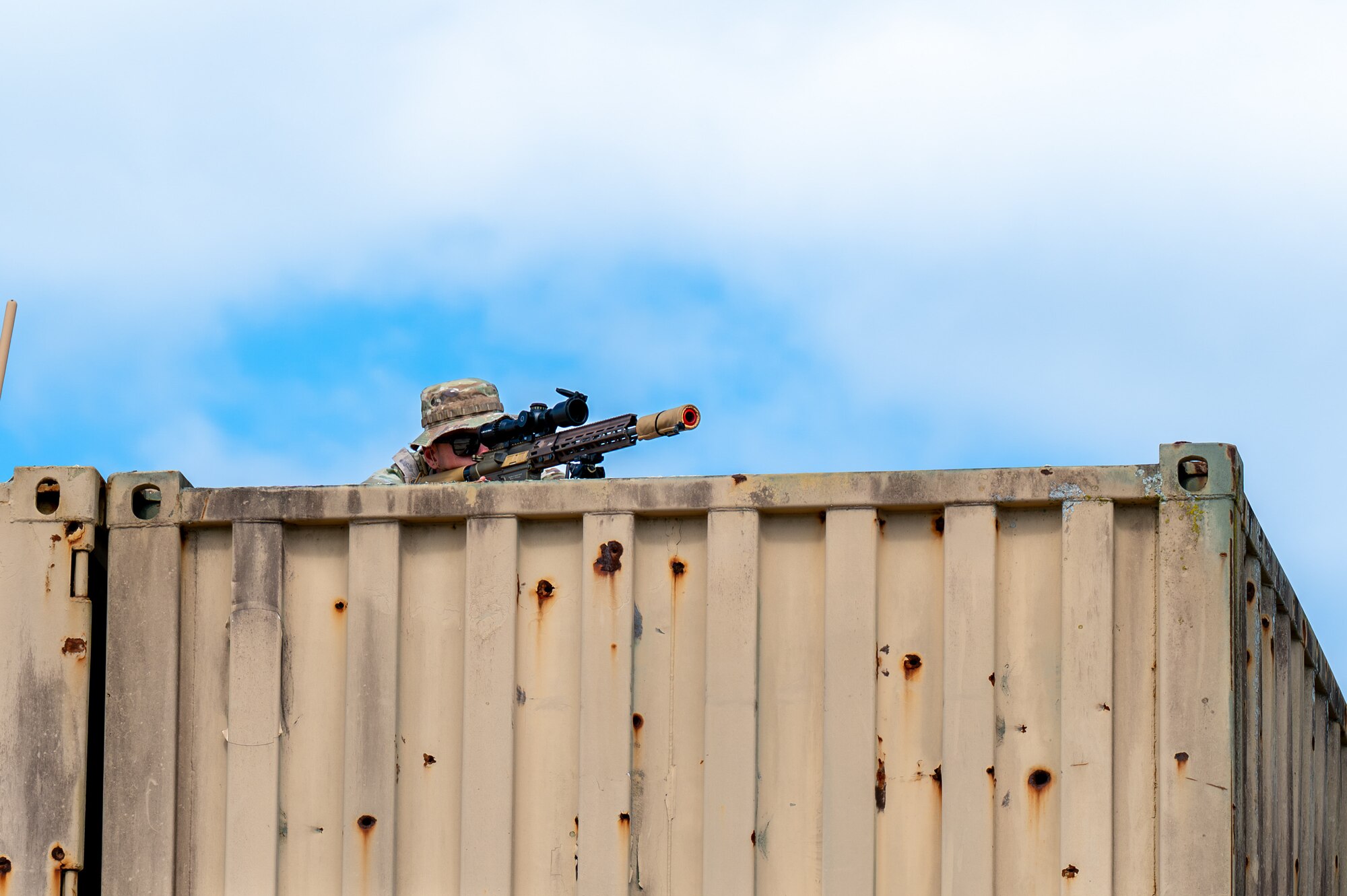 Man sits on the roof, looking through a scope.