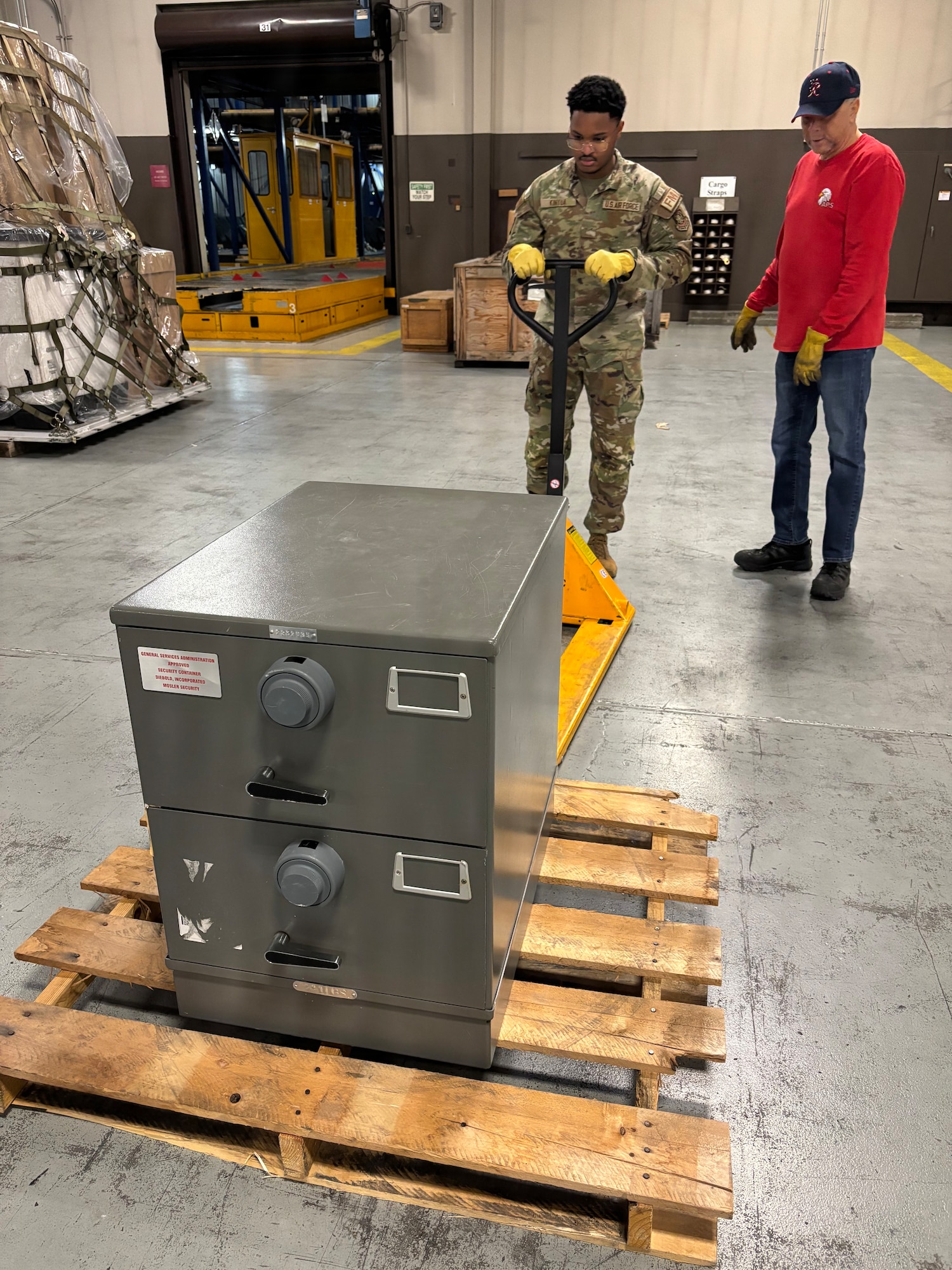 U.S. Airman 1st Class Wikiah Kinyua, 62d Comptroller Squadron financial operations technician, left, and Shawn Alexander, 62d Aerial Port Squadron deployment training program manager, move a palletized safe at Joint Base Lewis-McChord, Washington, January 22, 2026.