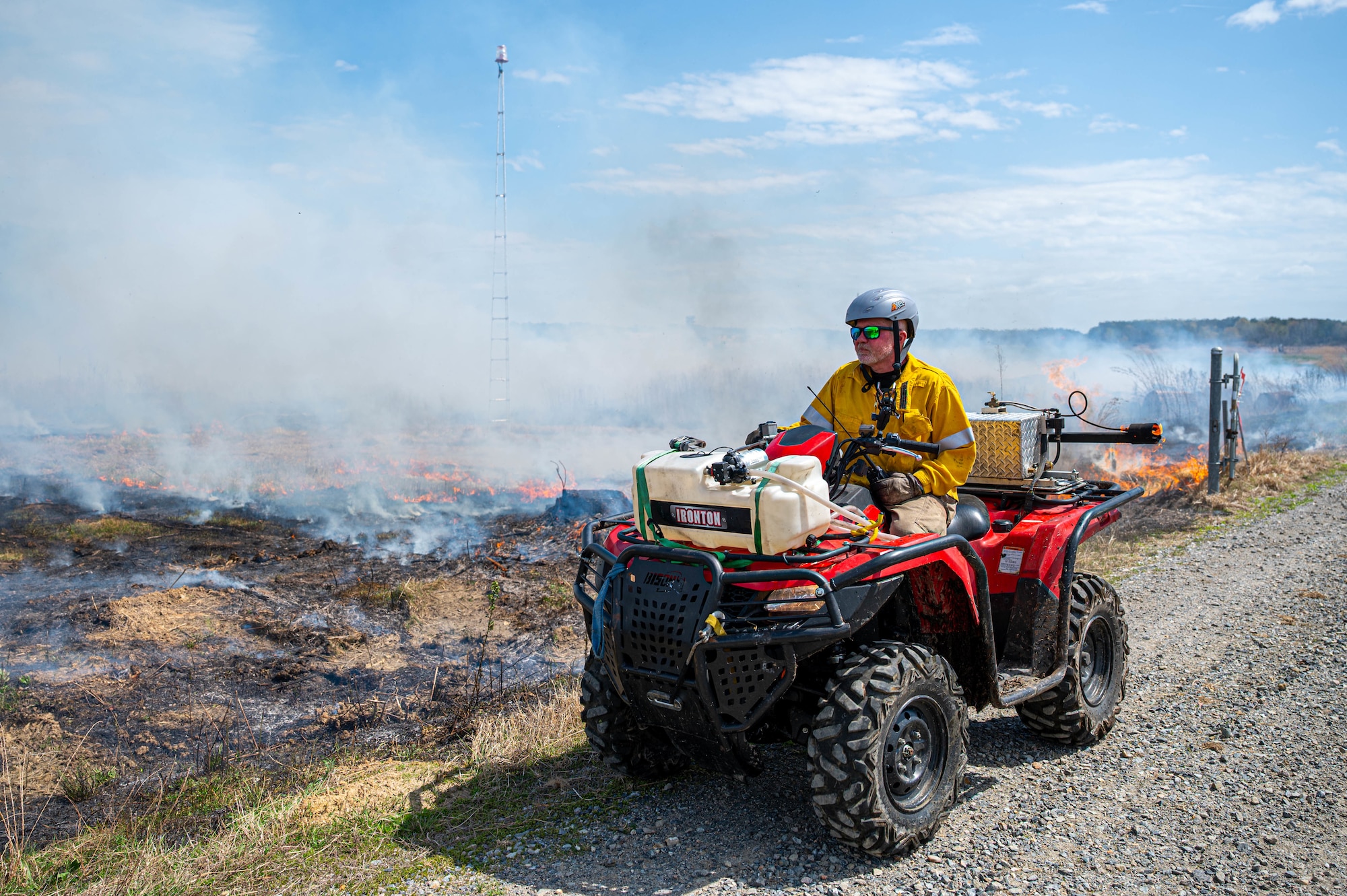 Shows a man on an off-road vehicle in front of smoke and brush.