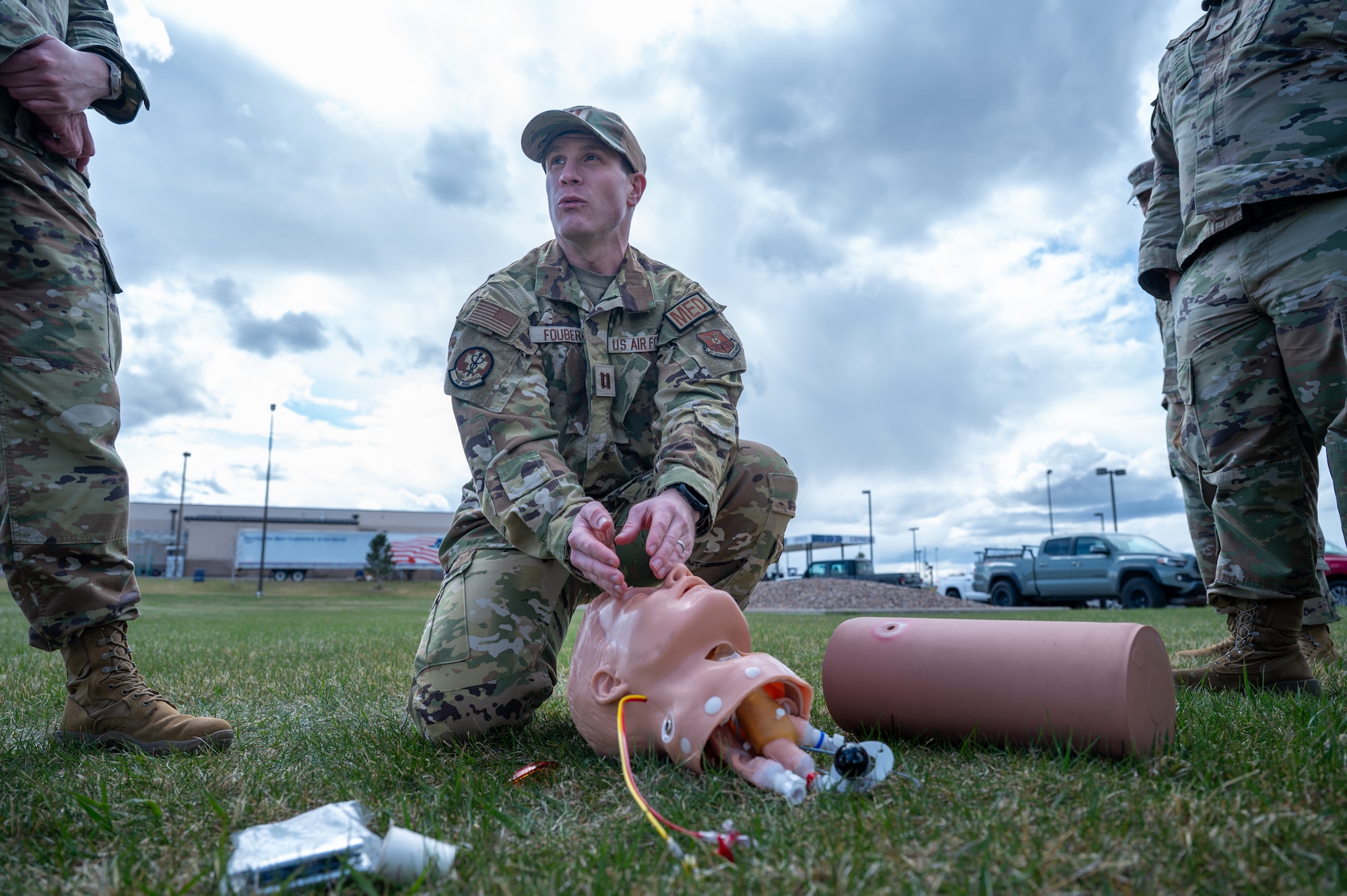 A uniformed instructor points to a simulated casualty head while teaching a group of Airmen during Tactical Combat Casualty Care training.
