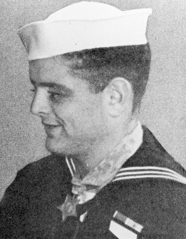 A man in a military dress uniform wearing a ribbon and medal smiles.
