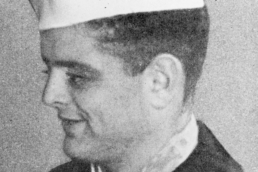 A man in a military dress uniform wearing a ribbon and medal smiles.