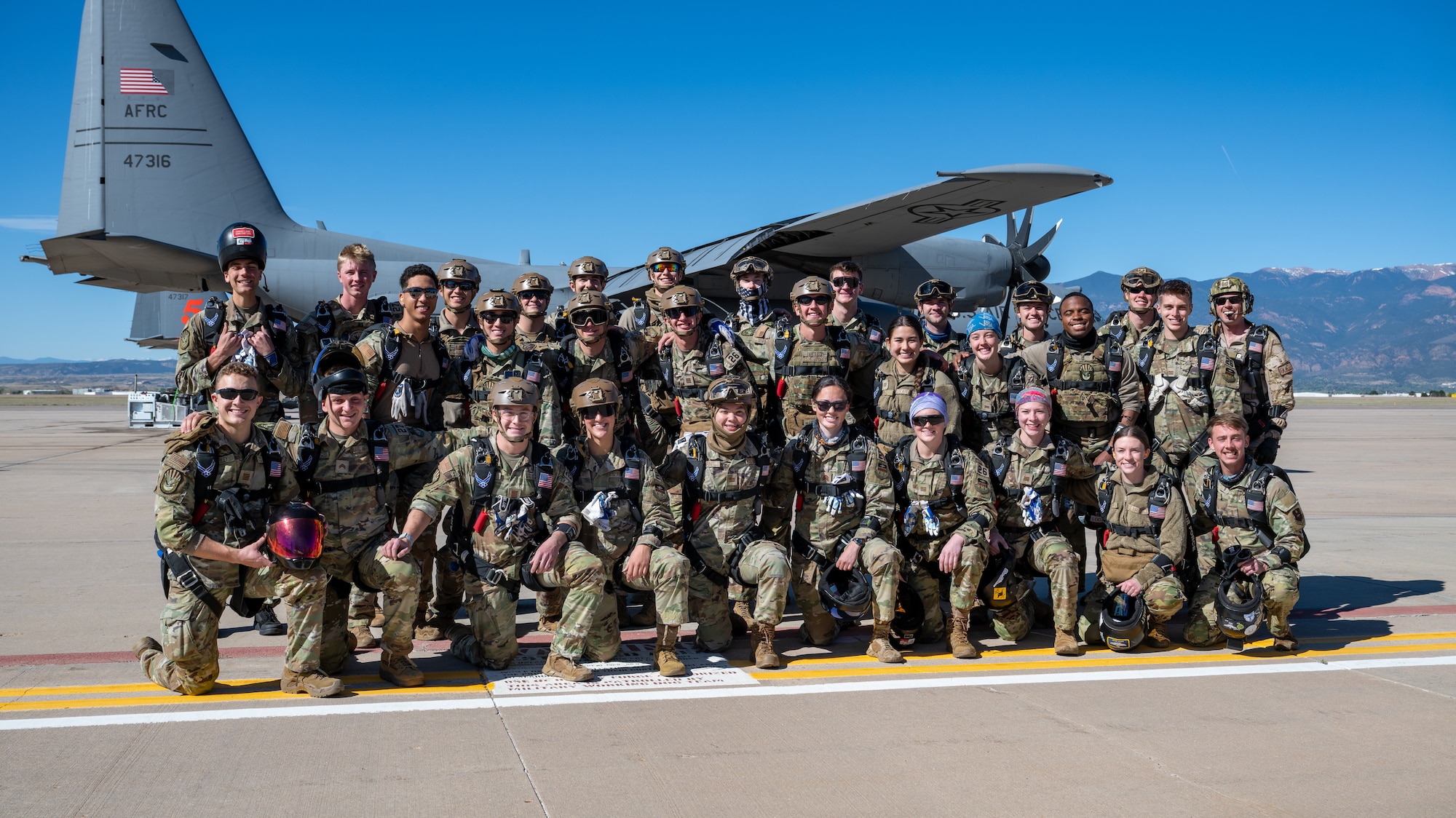 A large group of cadets line up on the flight line for a group photo in front of a C-130H Hercules aircraft.