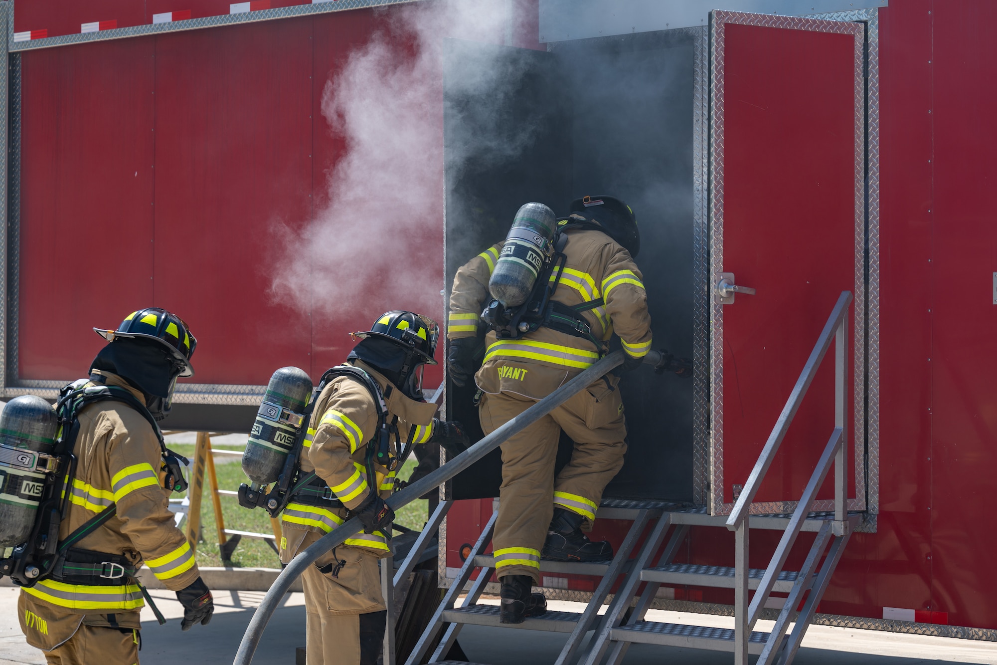 Arnold Air Force Base Fire and Emergency Services firefighters Joey Bryant, right, Matt Aussiker, center and Roger Whitton take part in  annual structure fire training April 15, 2026, outside the Arnold FES station at Arnold AFB, Tenn. A training unit, which resembles a two-story home, was again provided to Arnold AFB by the Kentucky Fire Commission, part of the Kentucky Community and Technical College System. Fires in the simulator are created through a propane-driven system, giving administrators greater control over the fires and providing trainees with improved safety when compared to other live fire training methods. Arnold FES firefighters are required to complete the live fire training annually per National Fire Protection Association and Air Force standards. (U.S. Air Force photo by Keith Thornburgh)