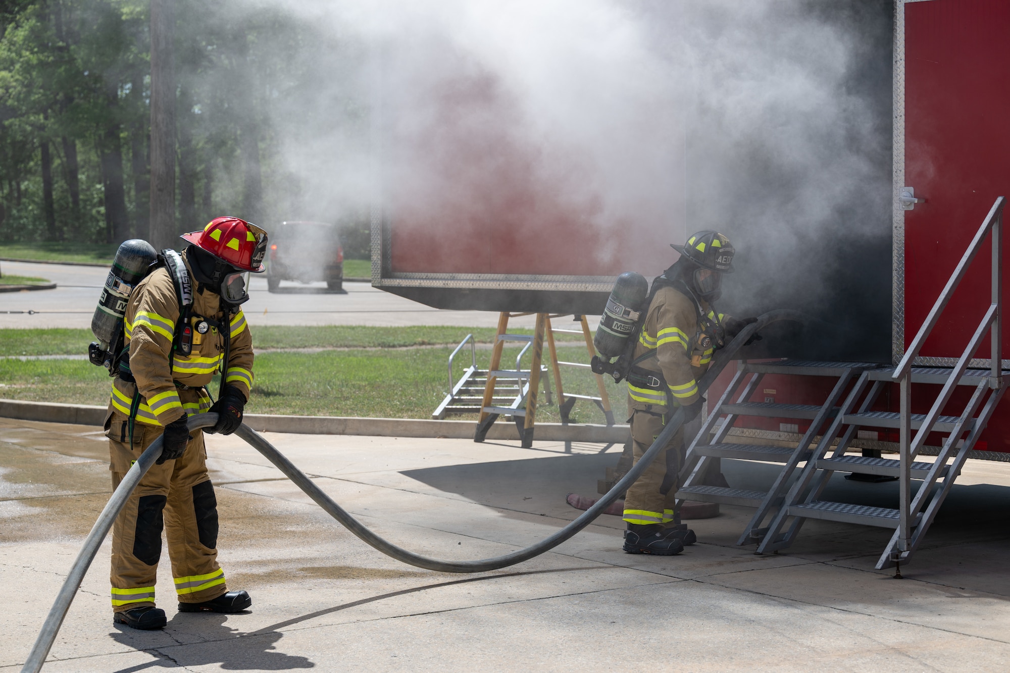 Arnold Air Force Base Fire and Emergency Services firefighters Roger Whitton, right, and Chris Graham take part in  annual structure fire training April 15, 2026, outside the Arnold FES station at Arnold AFB, Tenn. A training unit, which resembles a two-story home, was again provided to Arnold AFB by the Kentucky Fire Commission, part of the Kentucky Community and Technical College System. Fires in the simulator are created through a propane-driven system, giving administrators greater control over the fires and providing trainees with improved safety when compared to other live fire training methods. Arnold FES firefighters are required to complete the live fire training annually per National Fire Protection Association and Air Force standards. (U.S. Air Force photo by Keith Thornburgh)