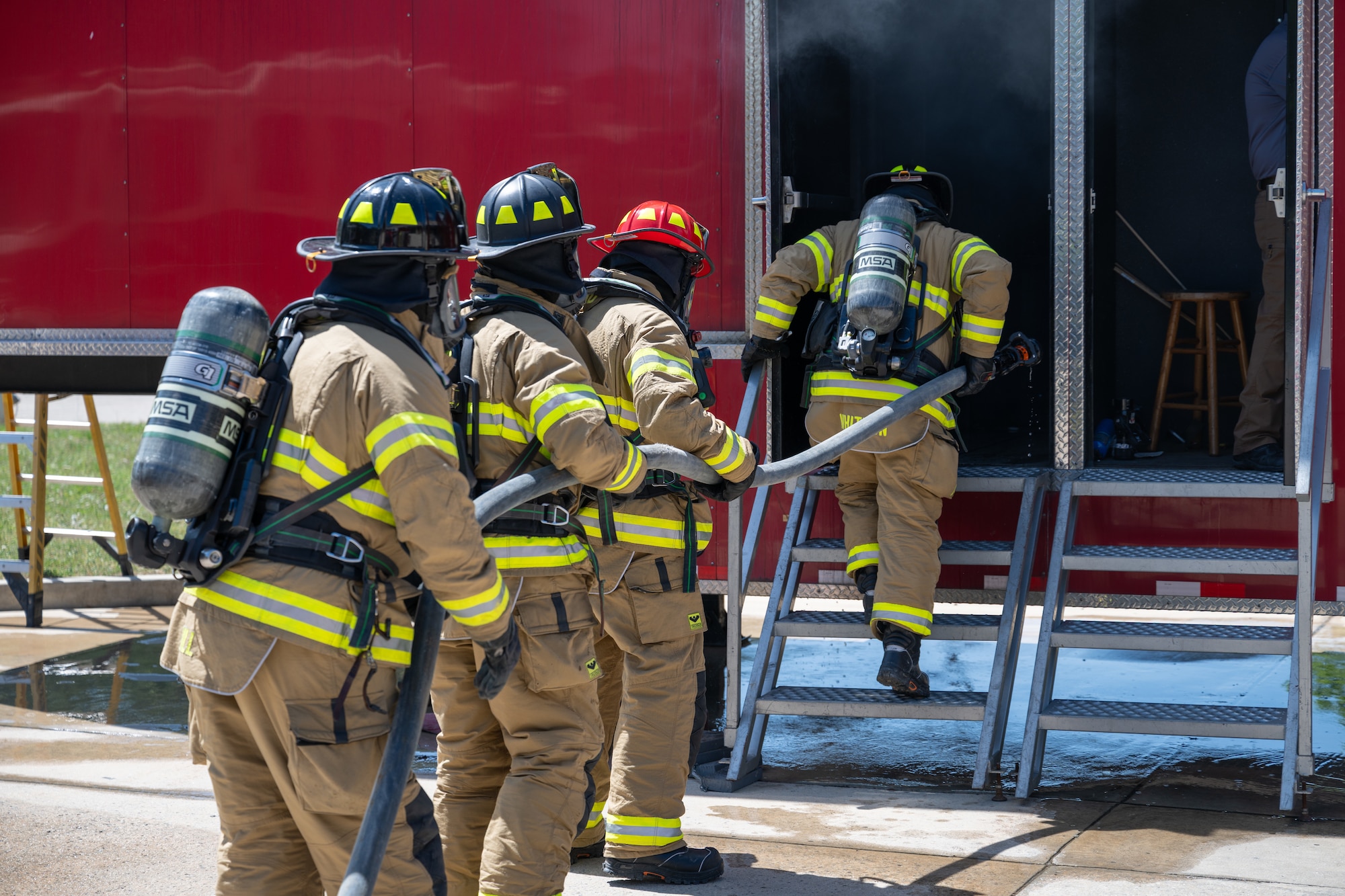 Arnold Air Force Base Fire and Emergency Services firefighters Roger Whitton, Chris Graham, Jason Montgomery and John Hill, from right, take part in  annual structure fire training April 15, 2026, outside the Arnold FES station at Arnold AFB, Tenn. A training unit, which resembles a two-story home, was again provided to Arnold AFB by the Kentucky Fire Commission, part of the Kentucky Community and Technical College System. Fires in the simulator are created through a propane-driven system, giving administrators greater control over the fires and providing trainees with improved safety when compared to other live fire training methods. Arnold FES firefighters are required to complete the live fire training annually per National Fire Protection Association and Air Force standards. (U.S. Air Force photo by Keith Thornburgh)