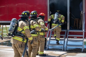 Arnold Air Force Base Fire and Emergency Services firefighters Roger Whitton, Chris Graham, Jason Montgomery and John Hill, from right, take part in  annual structure fire training April 15, 2026, outside the Arnold FES station at Arnold AFB, Tenn. A training unit, which resembles a two-story home, was again provided to Arnold AFB by the Kentucky Fire Commission, part of the Kentucky Community and Technical College System. Fires in the simulator are created through a propane-driven system, giving administrators greater control over the fires and providing trainees with improved safety when compared to other live fire training methods. Arnold FES firefighters are required to complete the live fire training annually per National Fire Protection Association and Air Force standards. (U.S. Air Force photo by Keith Thornburgh)