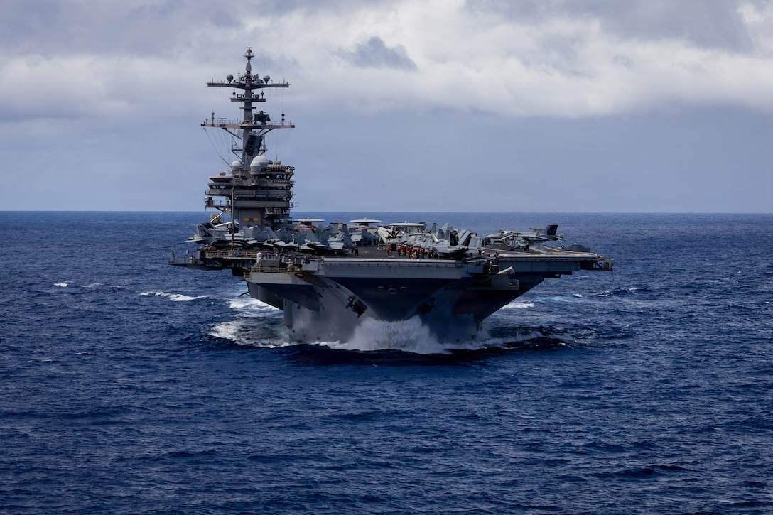 An aircraft carrier sails in the ocean, with the horizon in the background.