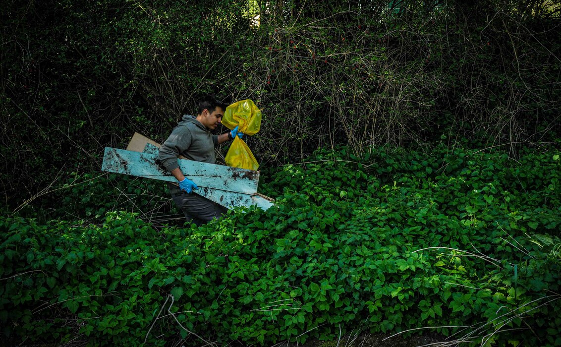 A volunteer carries a trash bag and discarded wooden planks through brush along the Spangerbach creek during the annual creek cleanup in Spangdahlem, Germany, April 25, 2026. Participants hauled collected debris back to the Spangdahlem volunteer fire department throughout the morning. (U.S. Air Force photo by Master Sgt. Alexander W. Riedel)